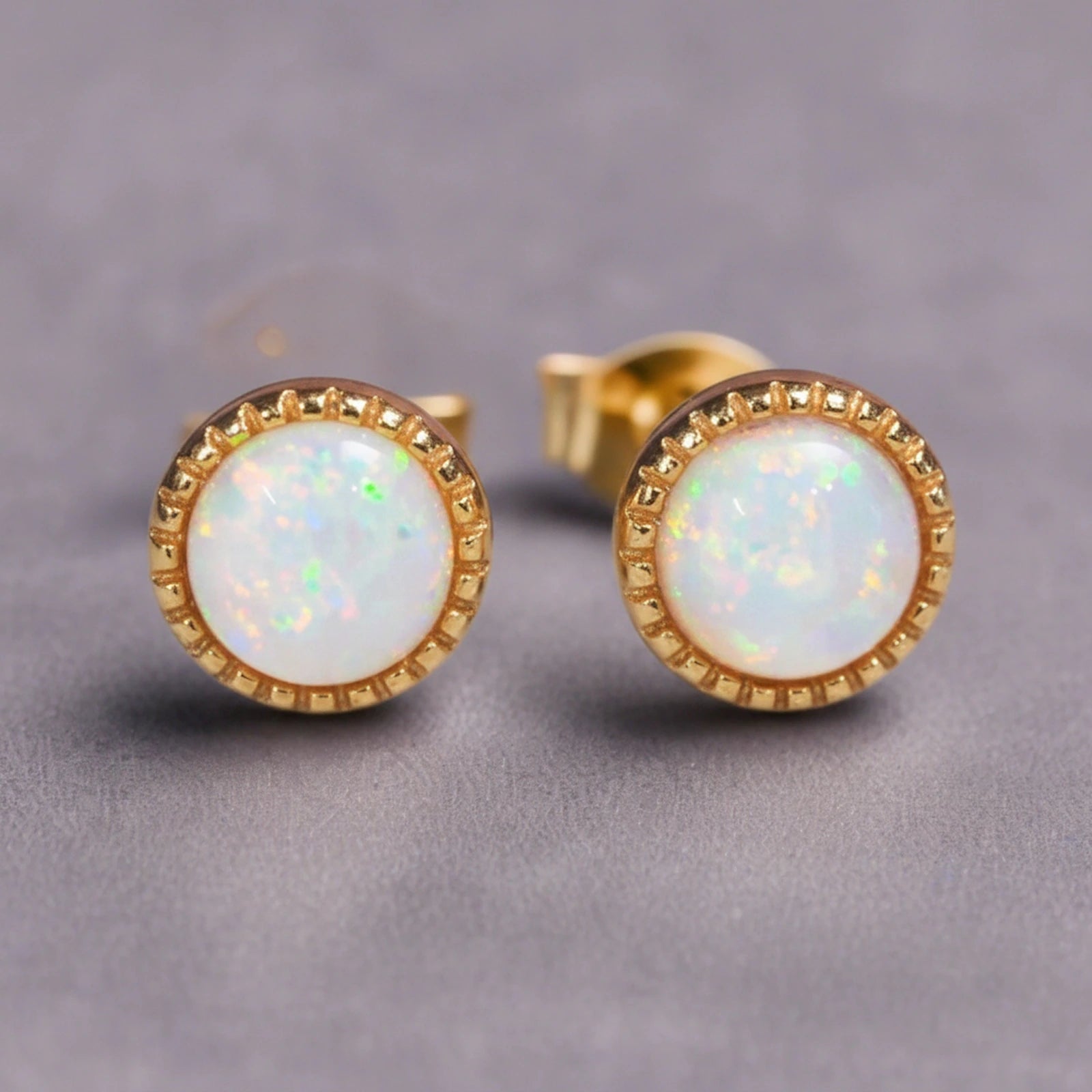 Gold White Opal stud earrings on a grey background.