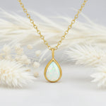 Gold necklace with a teardrop-shaped opal pendant on a light background