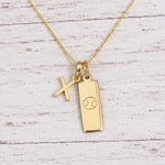 Gold Initial X Pendant and Cancer Zodiac Pendant Necklace on a fine gold chain against a light wooden background