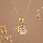 Gold initial X necklace with an April clear quartz teardrop on brown with dried flowers