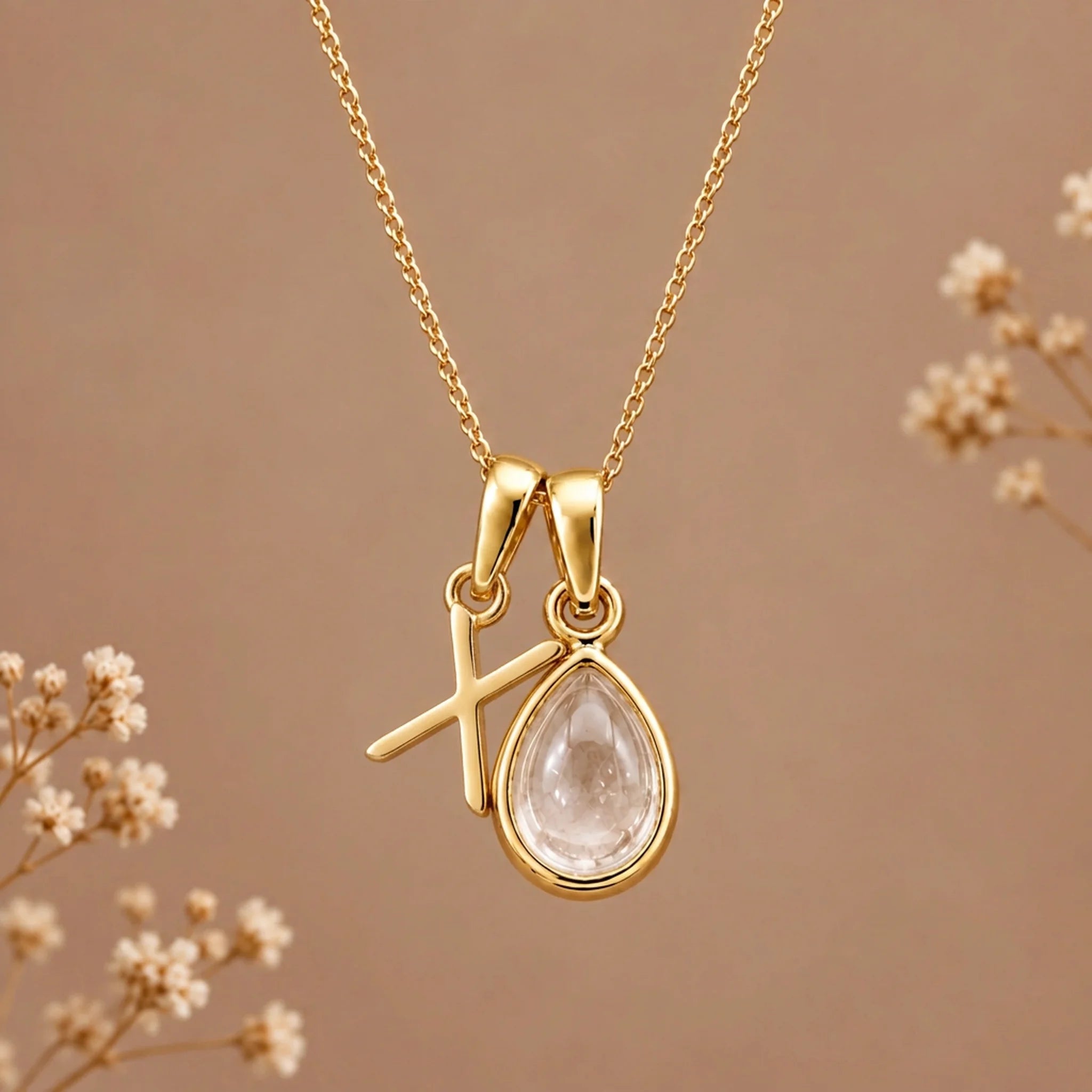 Gold initial X necklace with an April clear quartz teardrop on brown with dried flowers