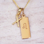 Gold X Initial and Leo Necklace on a fine gold chain against a light wooden background