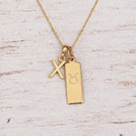 Gold X Initial and Taurus Necklace on a fine gold chain against a light wooden background