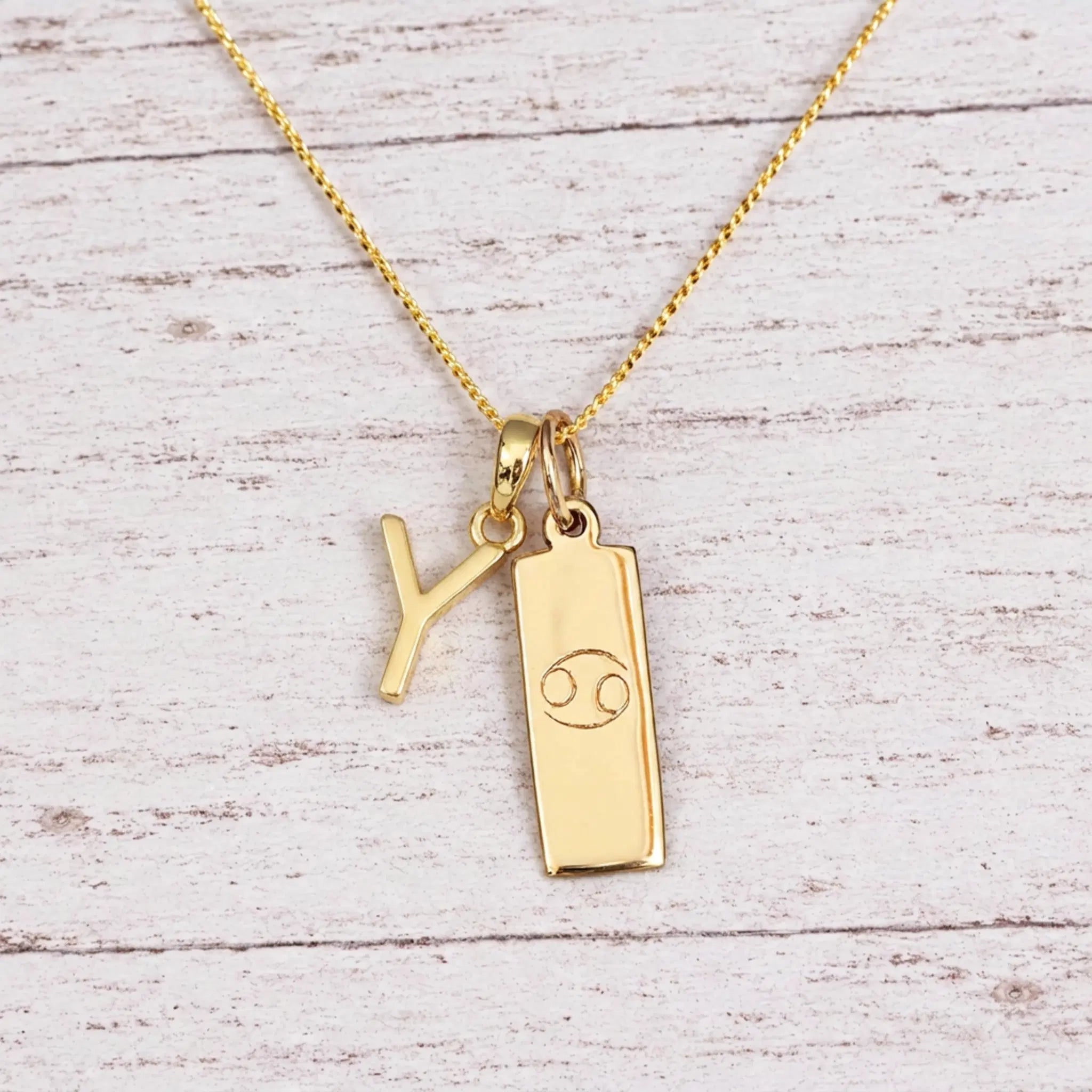 Gold Initial Y Pendant and Cancer Zodiac Pendant Necklace on a fine gold chain against a light wooden background