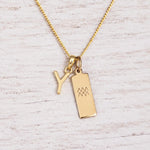 gold Y initial and aquarius zodiac necklace on fine gold chain against a light wooden background