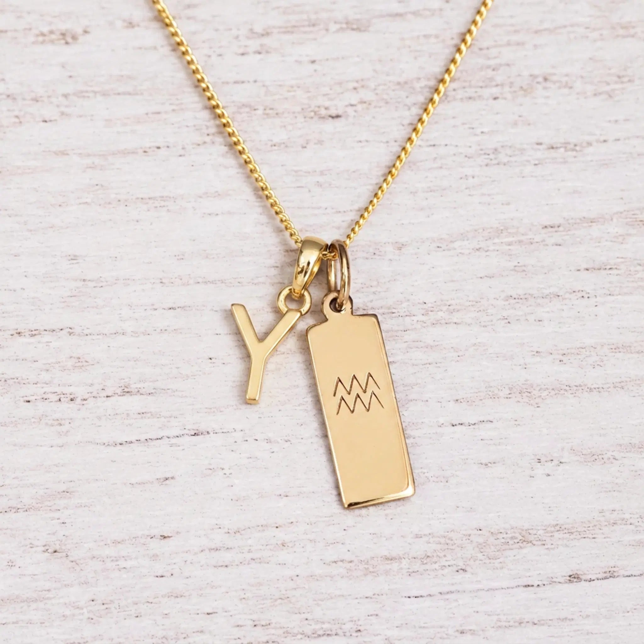 gold Y initial and aquarius zodiac necklace on fine gold chain against a light wooden background