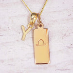 Gold initial and Libra zodiac necklace with a letter Y charm and engraved bar pendant on whitewashed wood