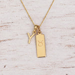 Gold Y Initial and Taurus Necklace on a fine gold chain against a light wooden background