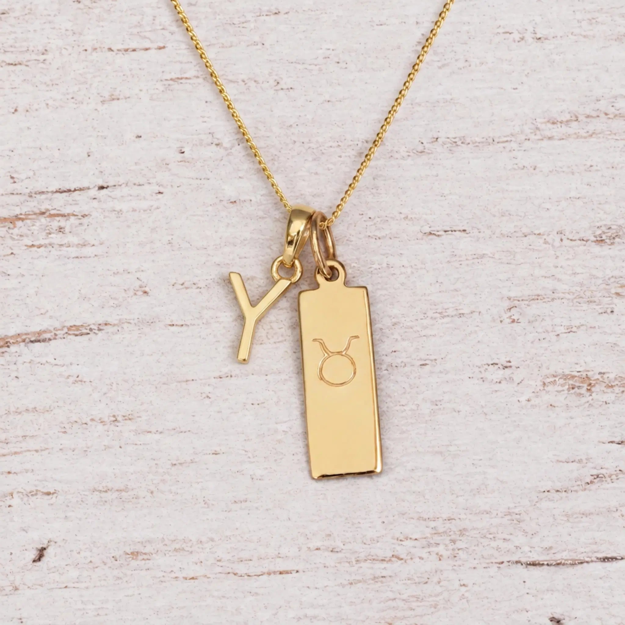 Gold Y Initial and Taurus Necklace on a fine gold chain against a light wooden background