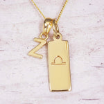 Gold initial and Libra zodiac necklace with a letter Z charm and engraved bar pendant on whitewashed wood