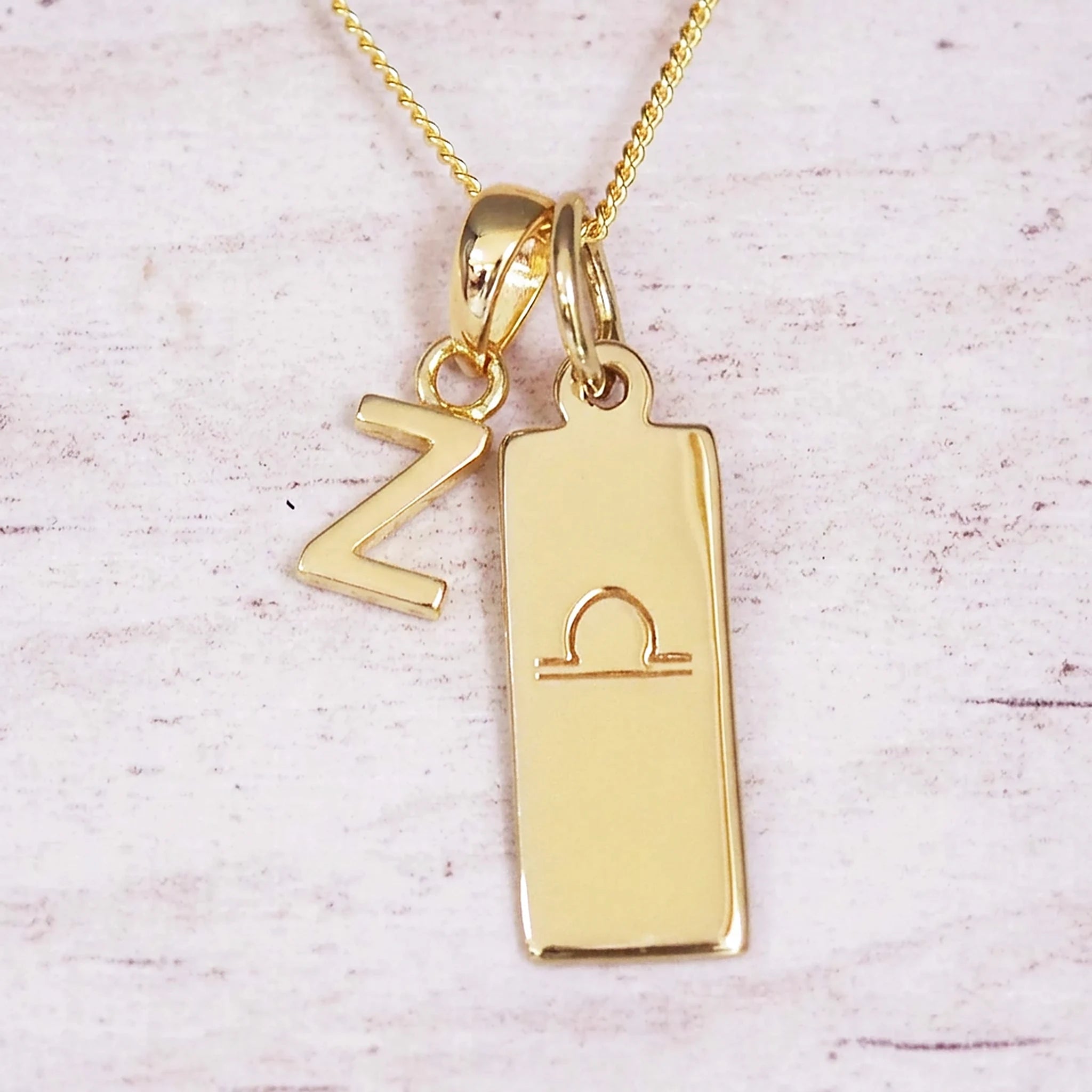 Gold initial and Libra zodiac necklace with a letter Z charm and engraved bar pendant on whitewashed wood