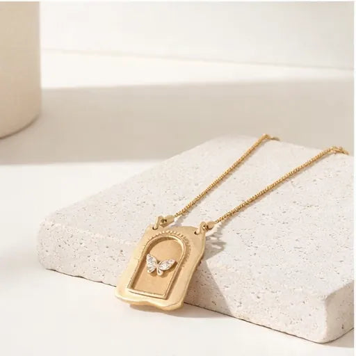 Gold necklace with a butterfly pendant on a white surface