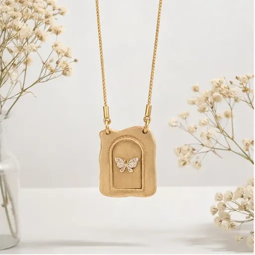Gold necklace with a butterfly pendant on a white background with dried flowers.