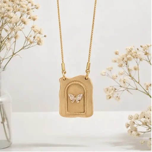 Gold necklace with a butterfly pendant on a white background with dried flowers.