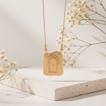 Gold necklace with a decorative pendant on a light surface with dried flowers.
