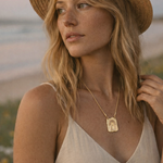 Woman wearing a straw hat and beige top with a necklace, standing outdoors.
