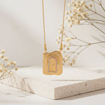Gold necklace with a decorative pendant on a light surface with dried flowers.