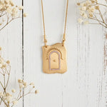 Gold necklace with a decorative pendant on a white wooden surface with flowers.
