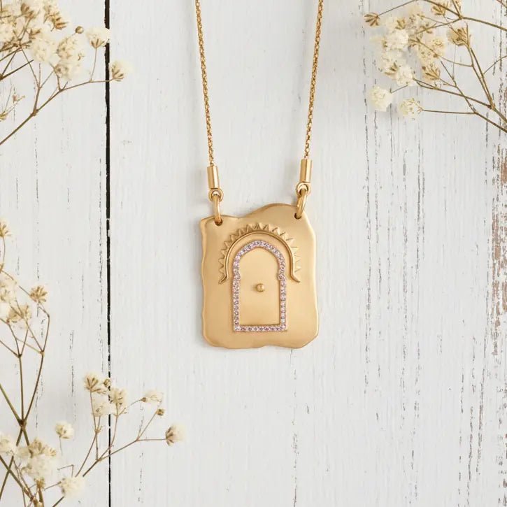 Gold necklace with a decorative pendant on a white wooden surface with flowers.