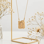 Gold necklace with a pendant on a gold stand, surrounded by dried flowers.