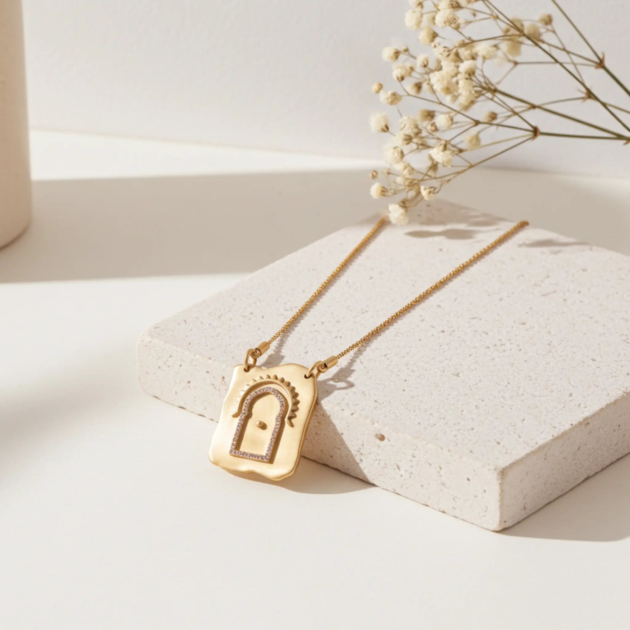 Gold necklace with a lock pendant on a light surface with dried flowers.
