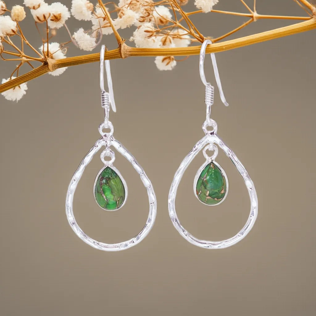 Silver earrings with green teardrop stones on a branch with small white flowers.