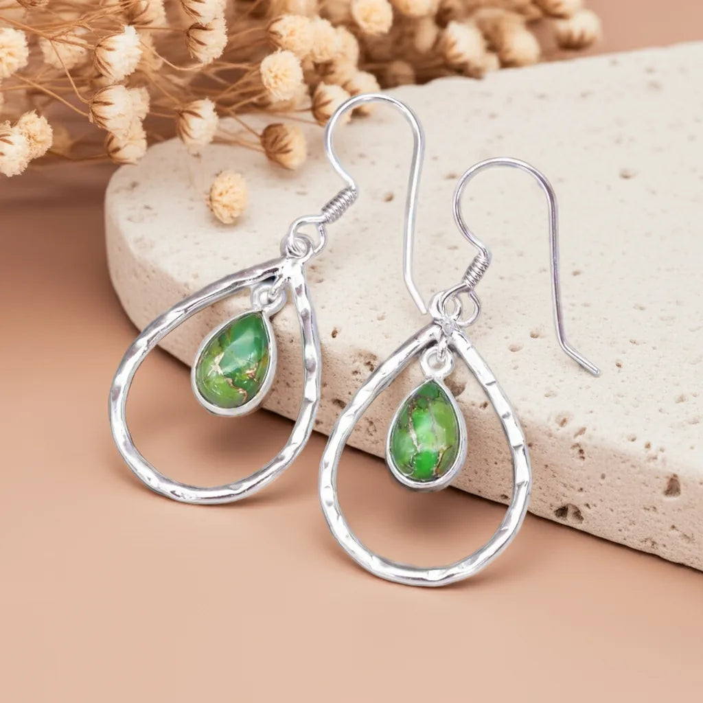 Silver earrings with green teardrop stones on a beige stone background