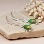 Silver earrings with green gemstones on a stone surface with dried flowers.