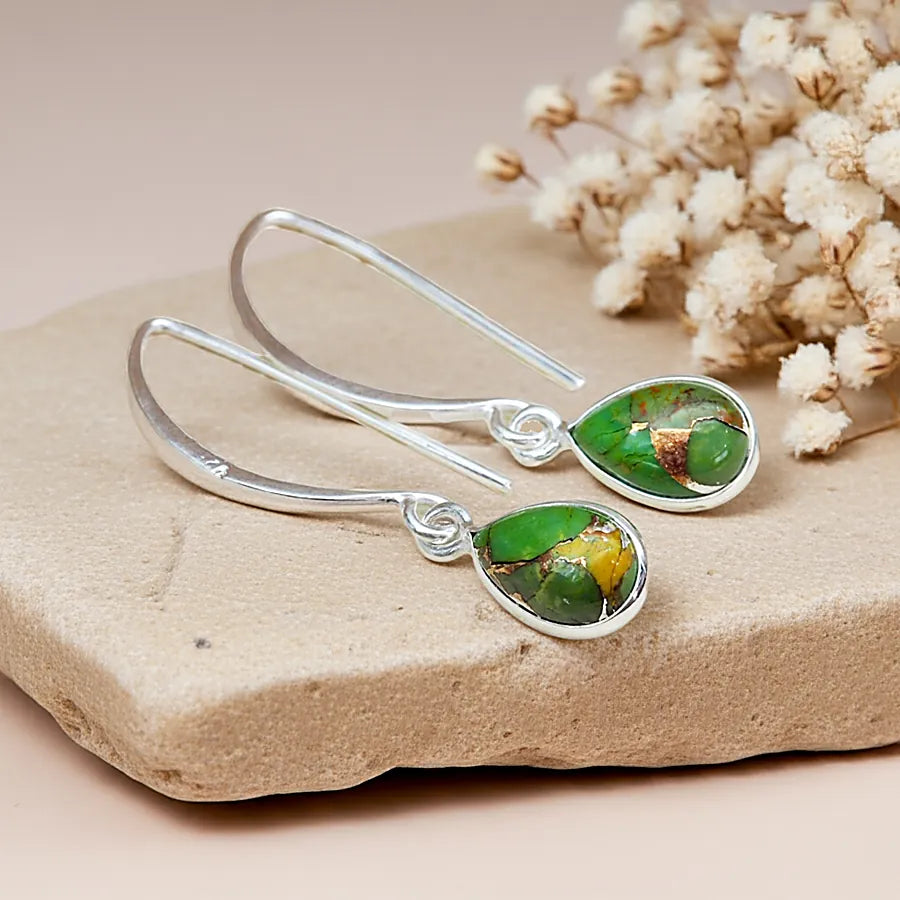 Silver earrings with green gemstones on a stone surface with dried flowers.