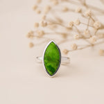 Silver ring with a marquise shaped bezel-set cabochon natural green turquoise gemstone on a beige background