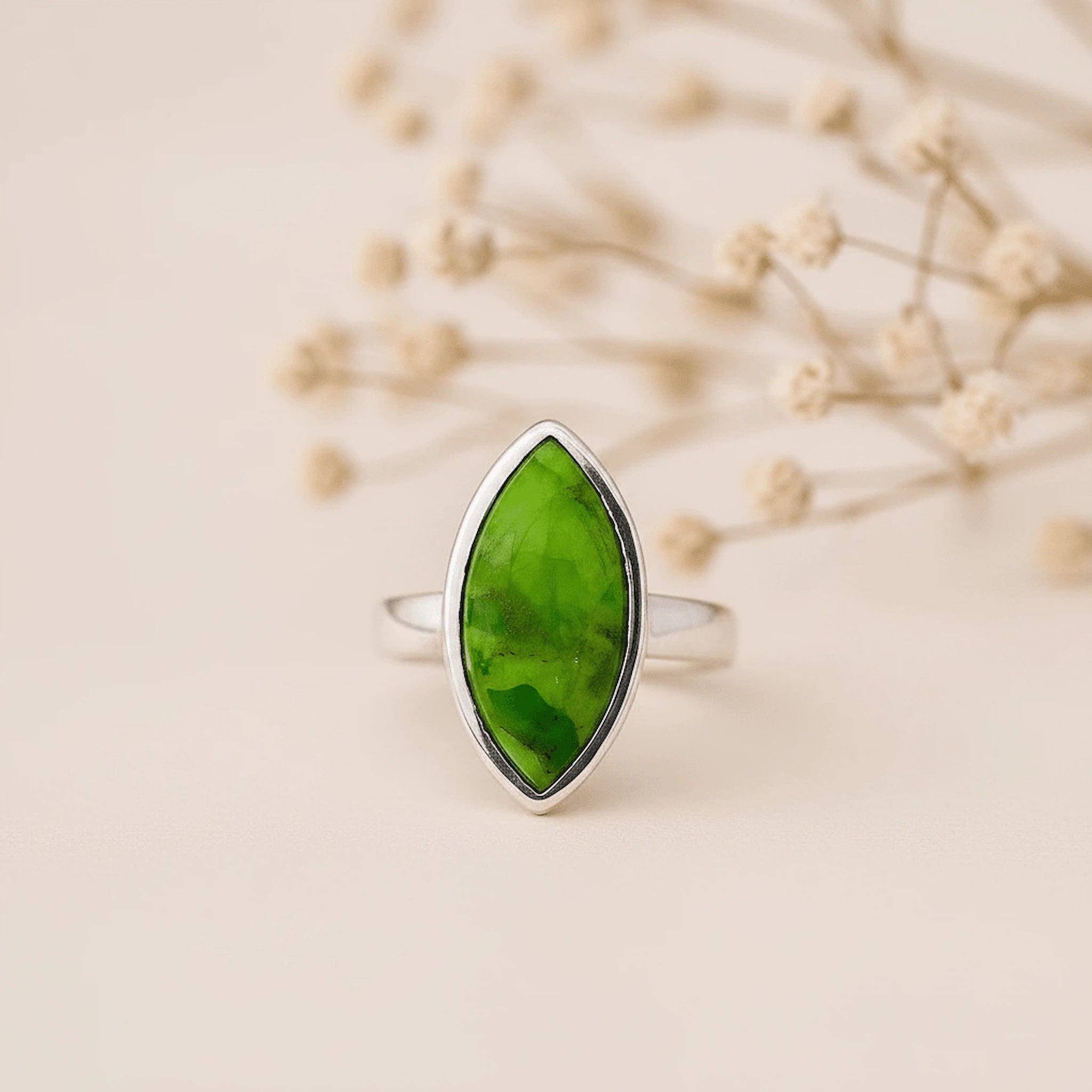 Silver ring with a marquise shaped bezel-set cabochon natural green turquoise gemstone on a beige background
