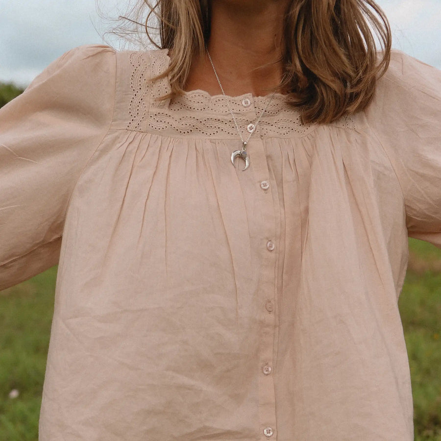 Woman in a field wearing a pink top and a crescent moon necklace with a rainbow moonstone in it. 