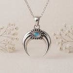 Silver crescent moon pendant with moonstone gemstone on a silver chain against a light background