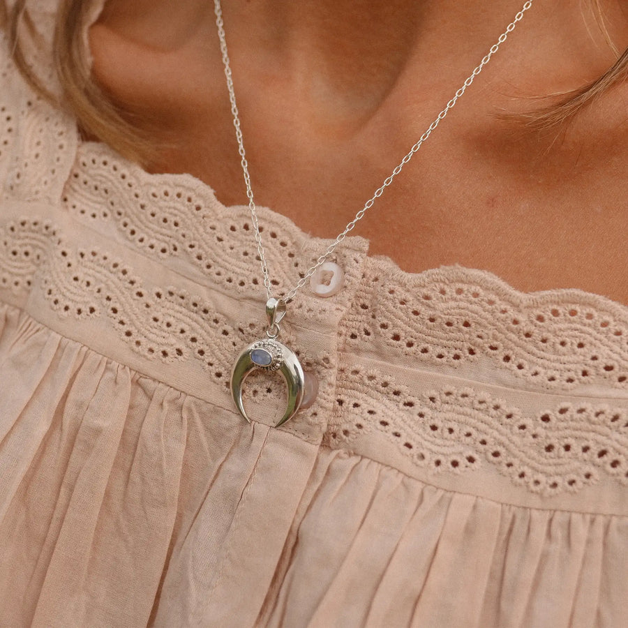 Woman wearing crescent shaped necklace with rainbow moonstone stone in the pendant.