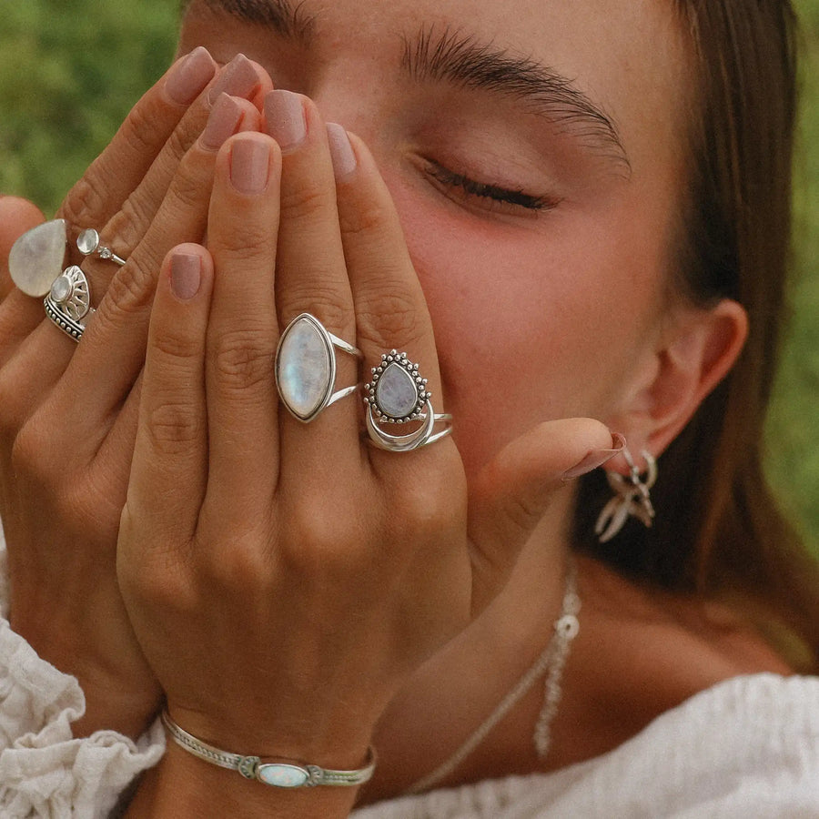 Woman with both hands covering her face, wearing two statement rainbow moonstone rings.