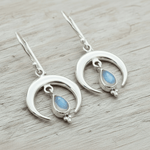 Silver moon-shaped earrings with teardrop moonstones on a wooden surface