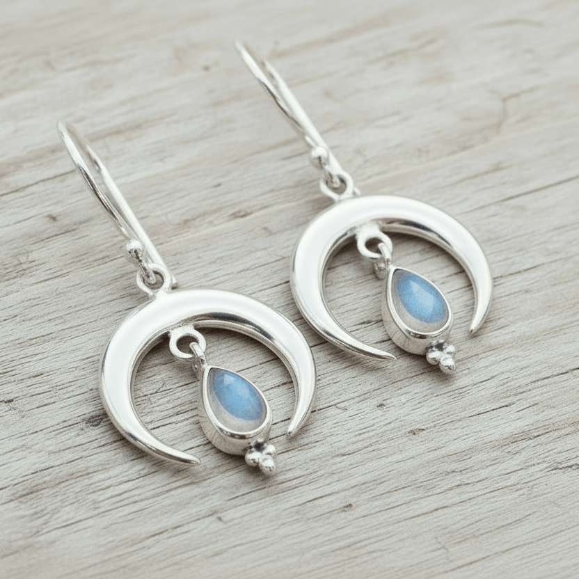 Silver moon-shaped earrings with teardrop moonstones on a wooden surface