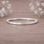 Sterling Silver thin hammered stacker ring on a wooden surface with delicate flowers in the background