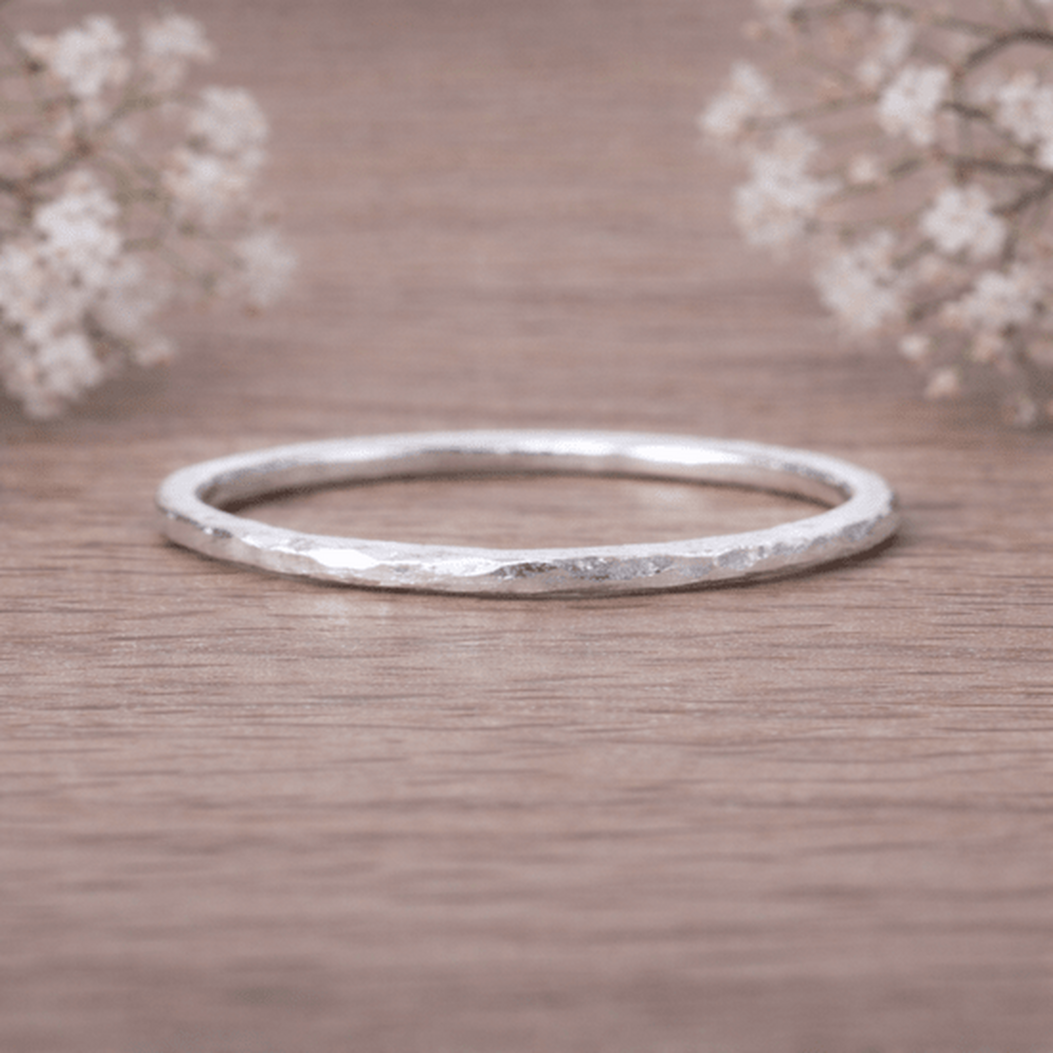 Sterling Silver thin hammered stacker ring on a wooden surface with delicate flowers in the background