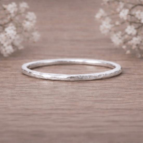 Sterling Silver thin hammered stacker ring on a wooden surface with delicate flowers in the background