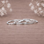 four silver rings with a hammered texture, stacked together on a wooden surface with soft-focus baby's breath flowers in the background.