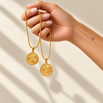 Hand holding two gold waterproof zodiac medallion necklaces
