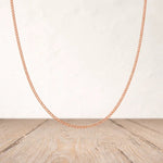 Rose gold chain necklace on a wooden surface with a light background