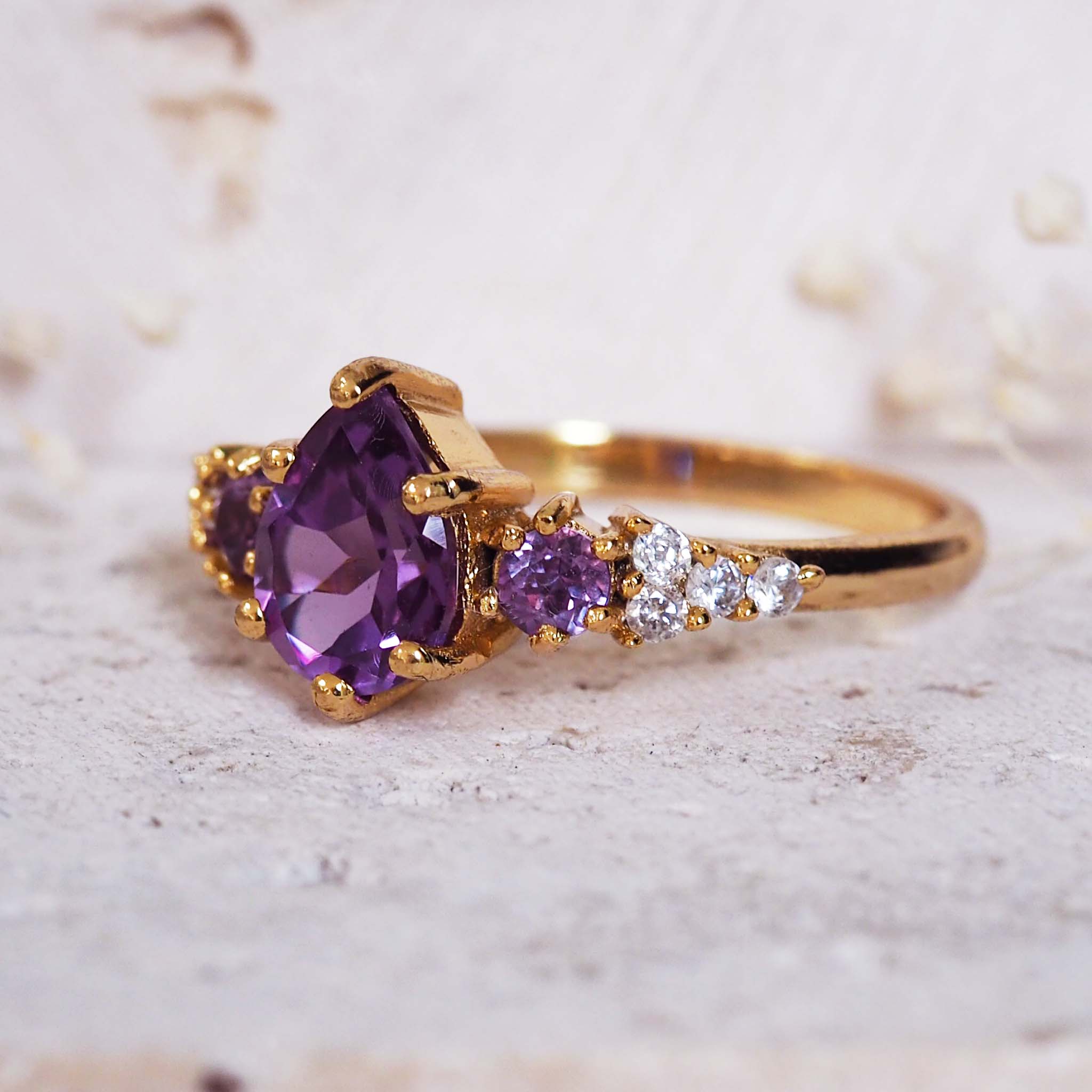 Gold ring with purple gemstone and smaller diamonds on a light background