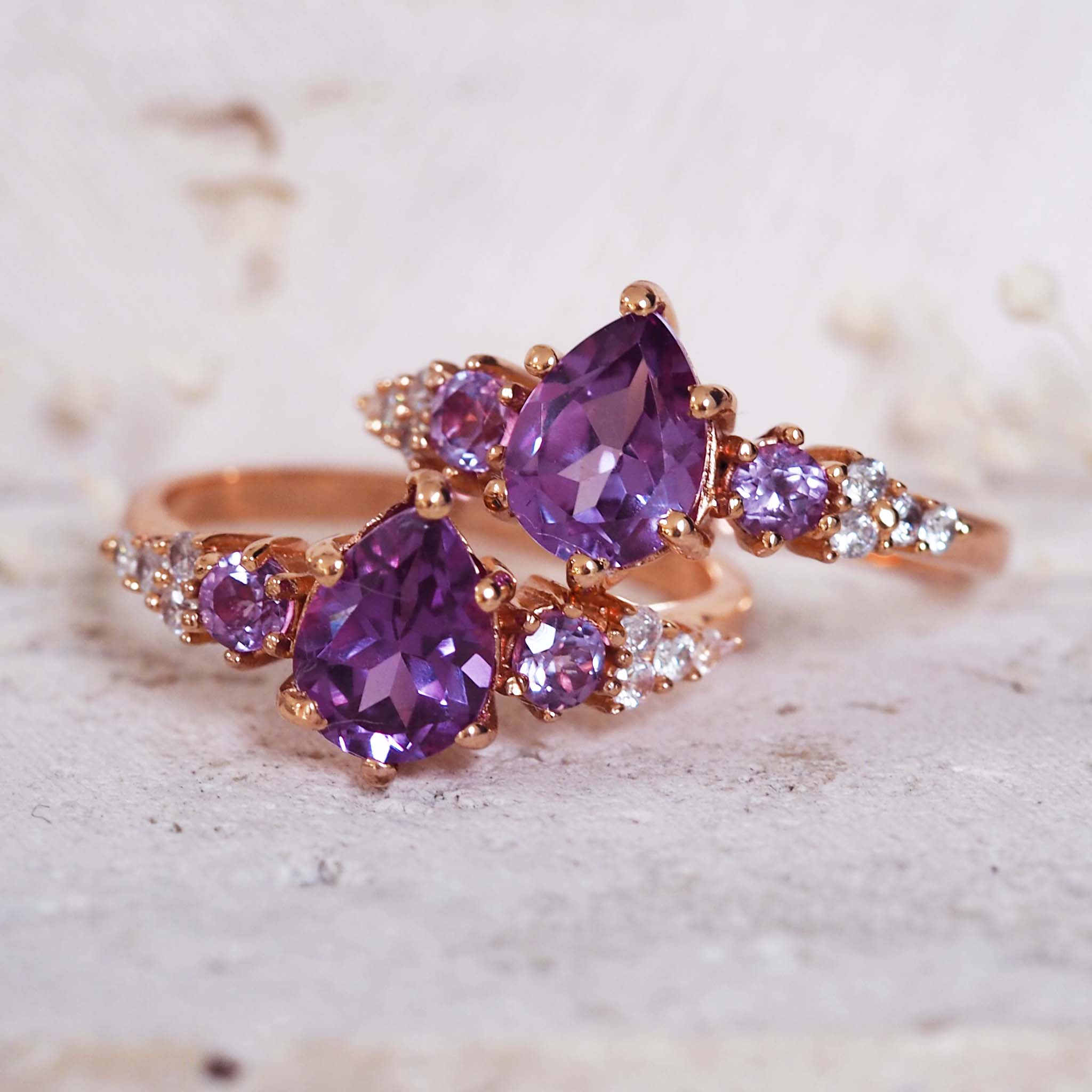 Rose gold ring with purple gemstones on a textured surface