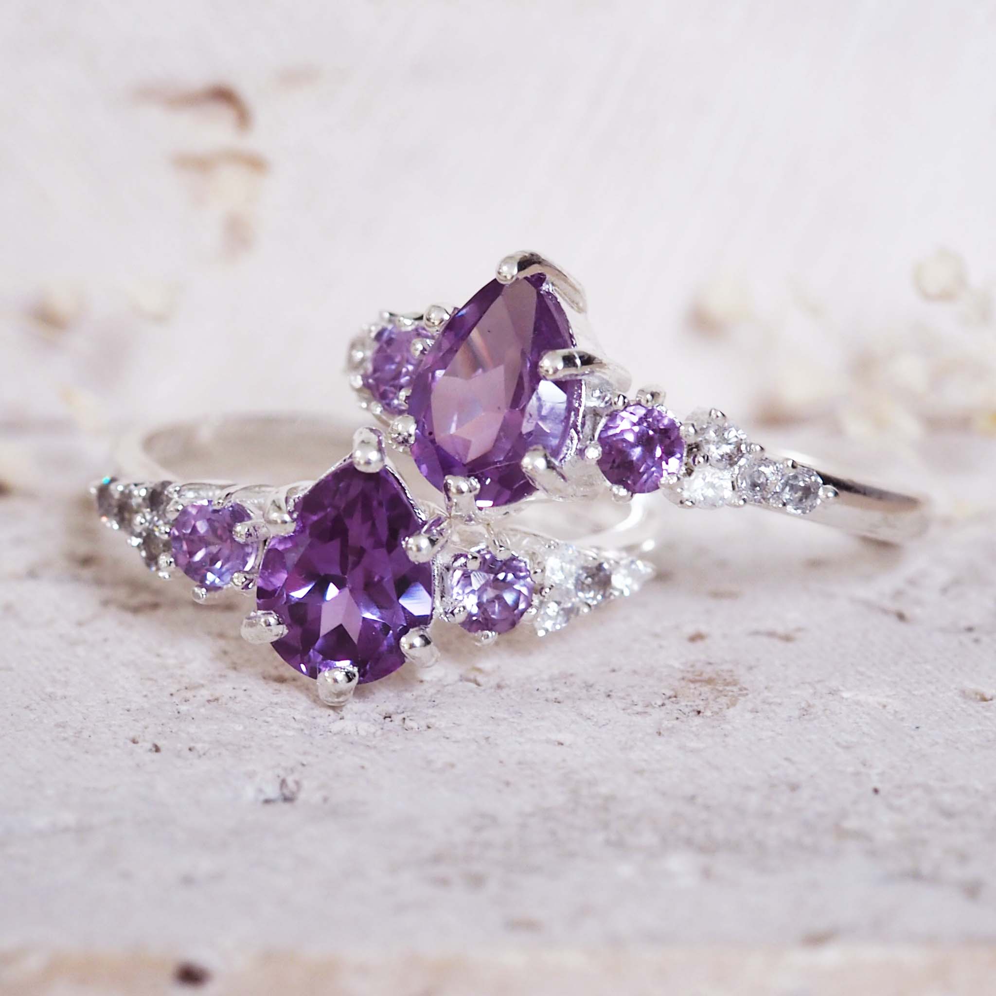 Purple gemstone ring with silver band on a textured surface