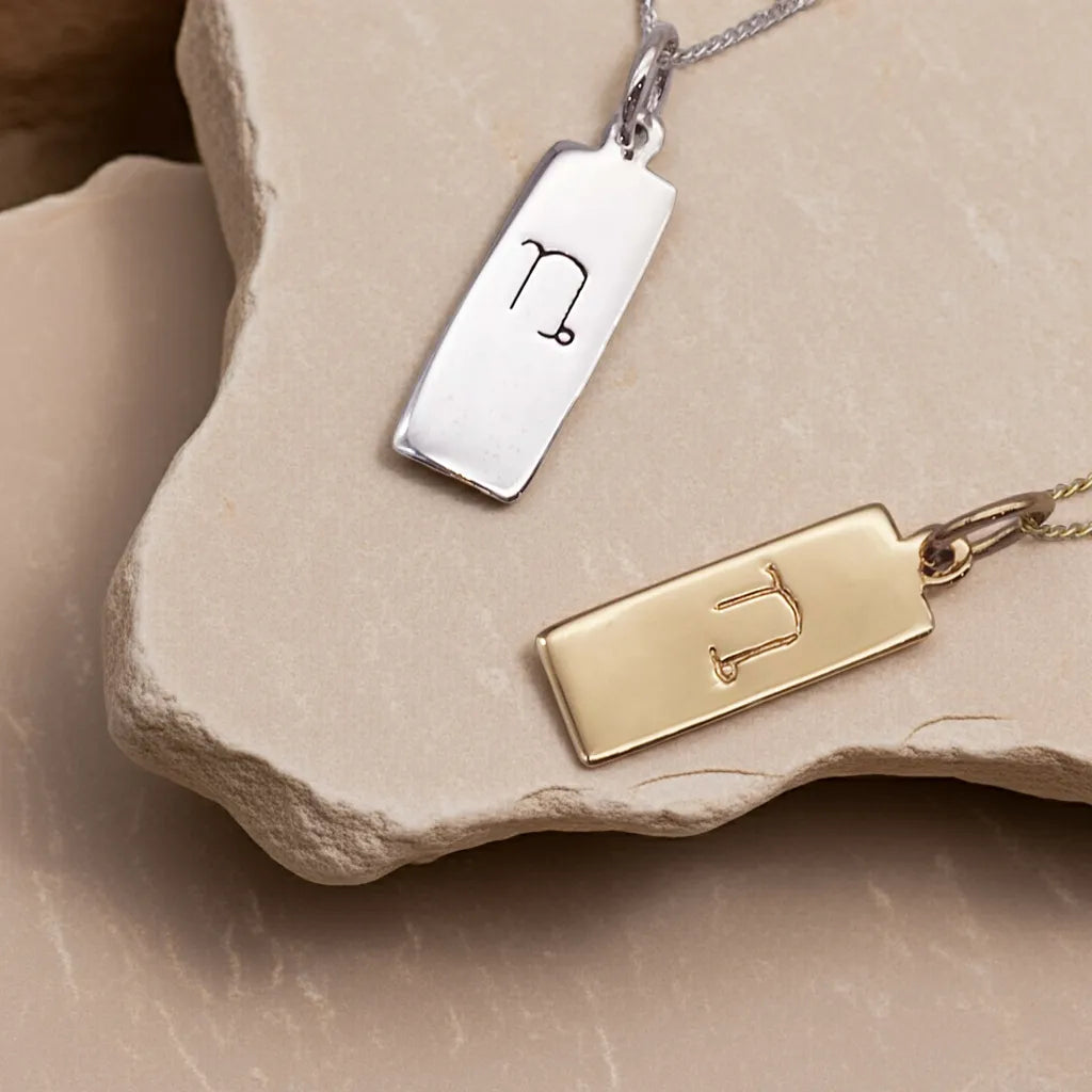 Gold and silver pendant necklaces with zodiac symbols on a stone surface