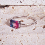 Silver ring with a multicolored gemstone on a textured beige surface
