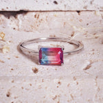 Silver ring with a rectangular multicolored gemstone on a textured beige surface