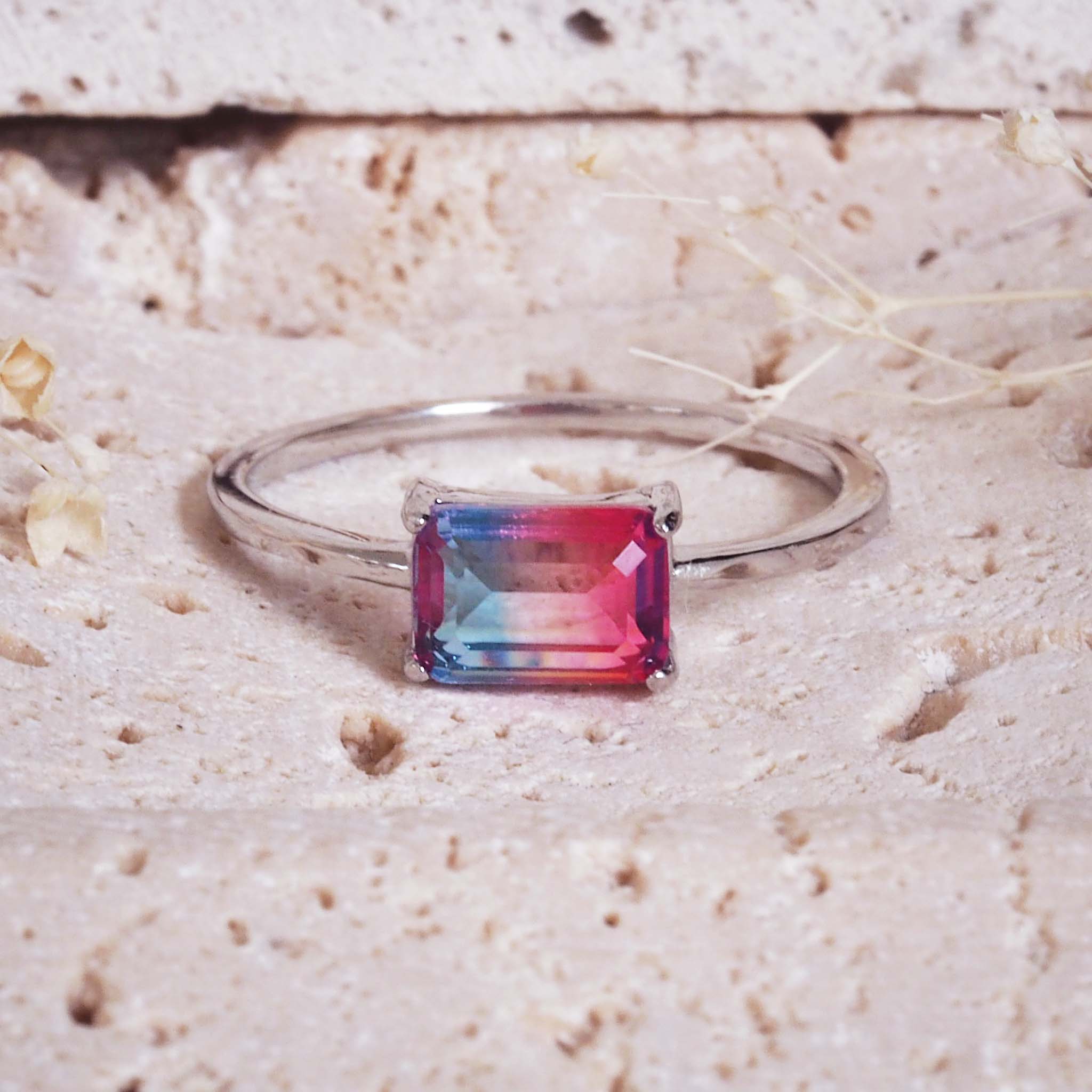 Silver ring with a rectangular multicolored gemstone on a textured beige surface